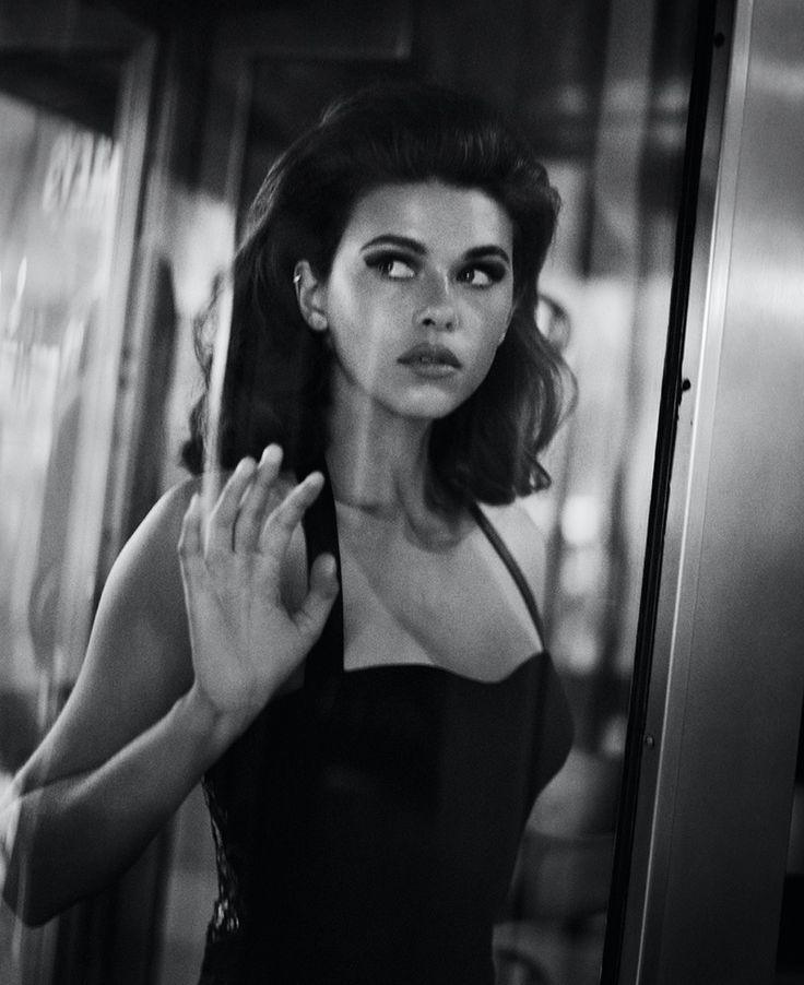 Black and white photo of a woman in a sleek going-out look standing at a glass door, illustrating DARK Femme's bold style