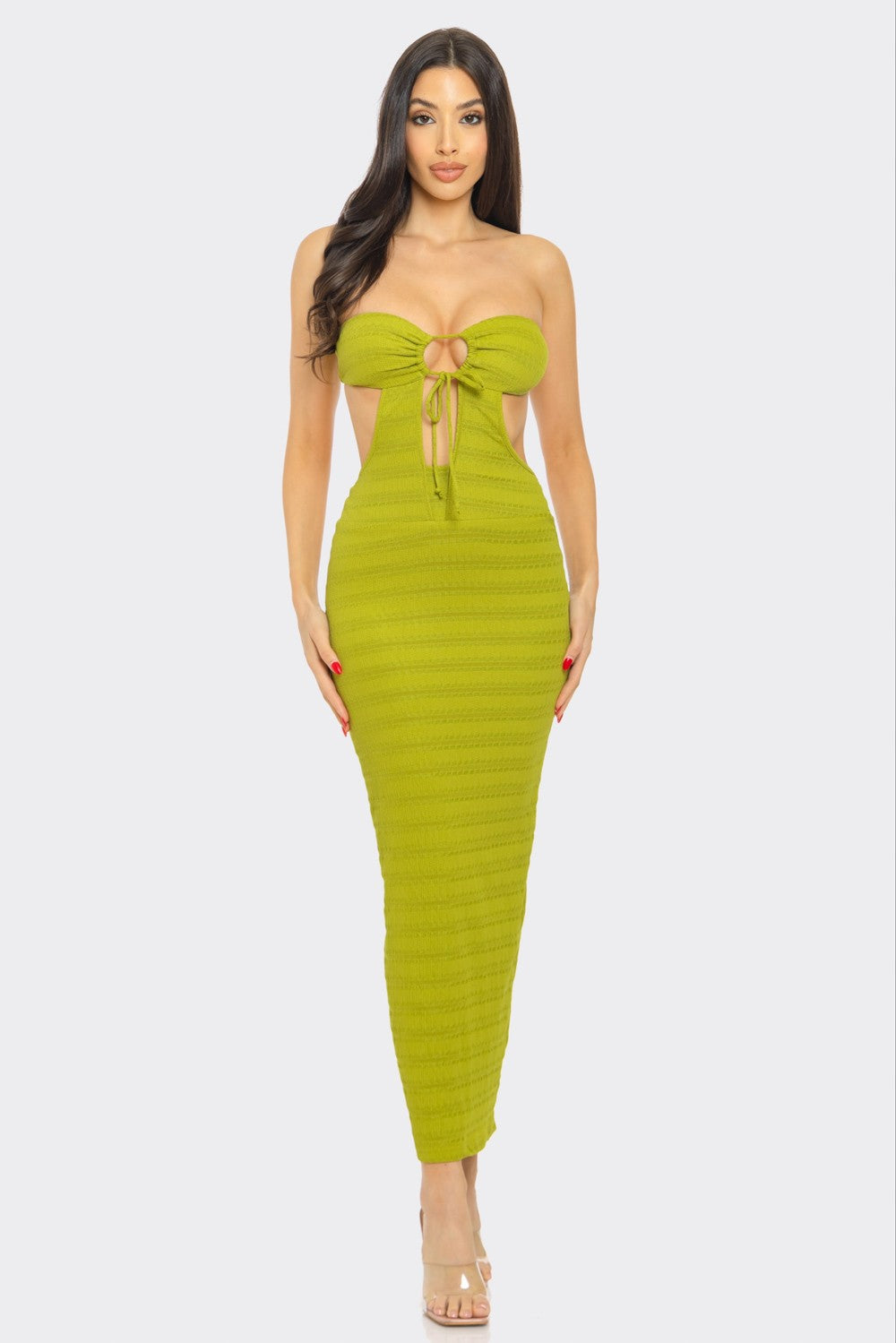 A woman with long dark hair poses against a white background, wearing a bright yellow strapless maxi dress with a front tie detail and cutout. She pairs the dress with clear high heels. 