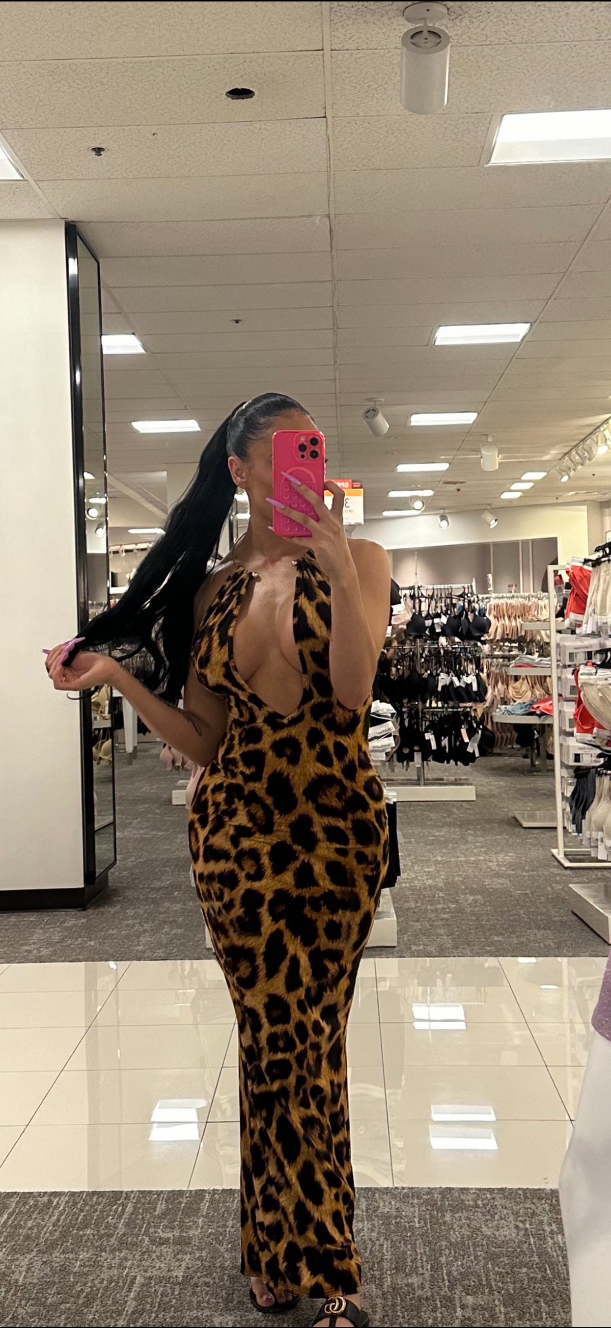 Rear view of a model in a golden leopard print halter maxi dress with an open back and floor-length bodycon fit, photographed in a store mirror