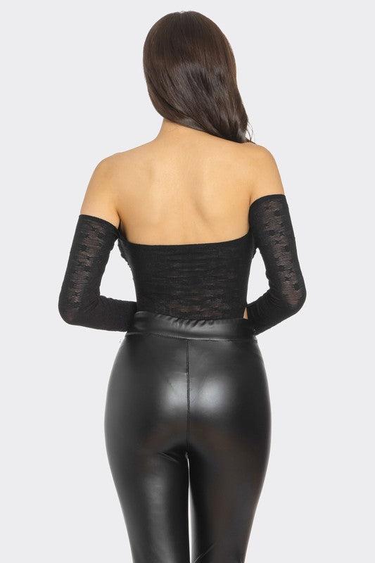 Back view of a model wearing a black off-shoulder lace bodysuit paired with black high-waisted faux leather pants. The lace fabric is semi-sheer, showcasing intricate patterns, while the outfit contours her silhouette, exuding a confident and sexy vibe.